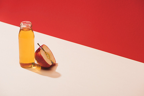 fresh juice in bottle near apple half on red background