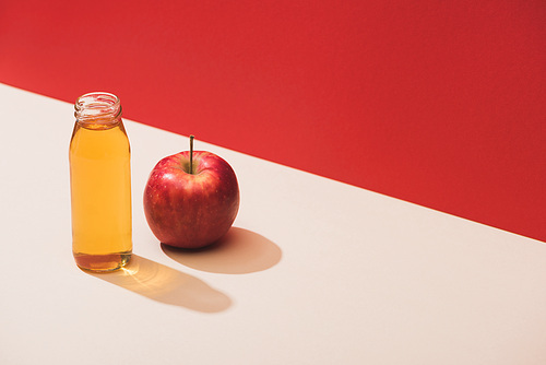 fresh juice in bottle near apple on red background