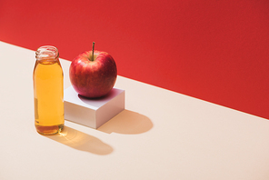 fresh juice in bottle near apple and white cube on red background