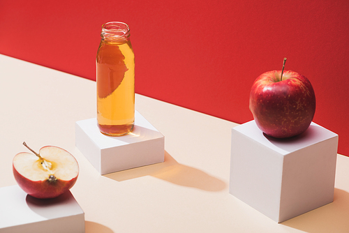 fresh juice in bottle near apples and white cubes on red background