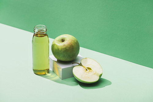 fresh juice near apples and and white cube on green and turquoise background
