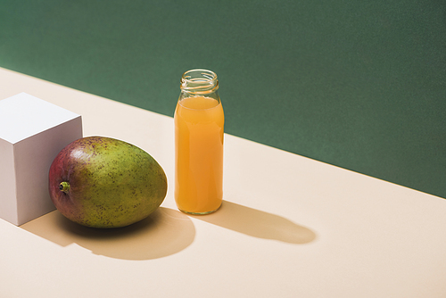 fresh juice in bottle near mango and white cube on green background