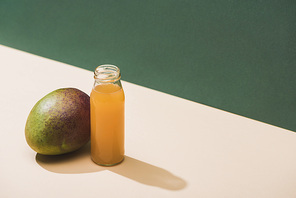 fresh juice in bottle near mango on green background