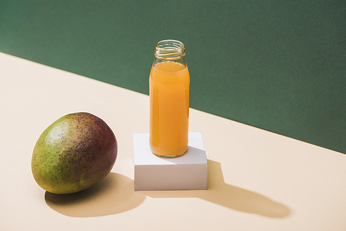 fresh juice in bottle near mango and white cube on green background