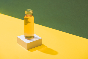 fresh juice in bottle on white cube on green and yellow background