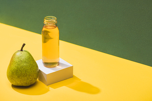 fresh juice in bottle near pear and white cube on green and yellow background