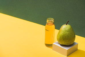 fresh juice in bottle near pear and white cube on green and yellow background