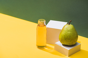 fresh juice in bottle near pear and white cubes on green and yellow background
