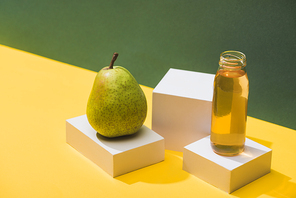 fresh juice in bottle near pear and white cubes on green and yellow background