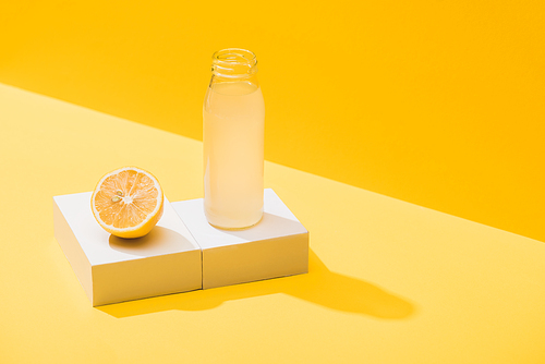 fresh juice in bottle near lemon half and white cube on yellow background