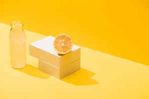 fresh juice in bottle near lemon and white cubes on yellow background