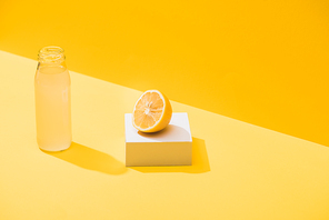 fresh juice in bottle near lemon half and white cube on yellow background
