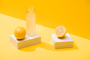 fresh juice in bottle near lemons and white cubes on yellow background