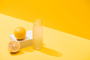 fresh juice in bottle near lemons and white cube on yellow background