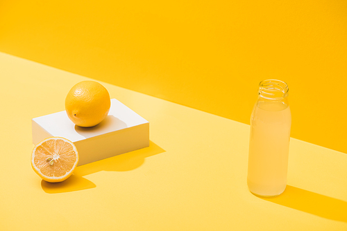 fresh juice in bottle near lemons and white cube on yellow background