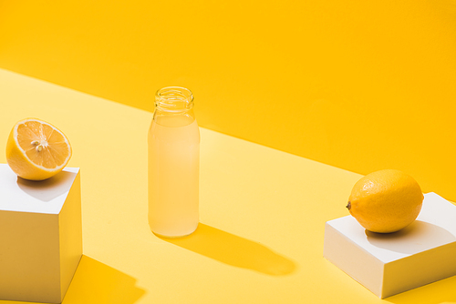 fresh juice in bottle near lemons and white cubes on yellow background