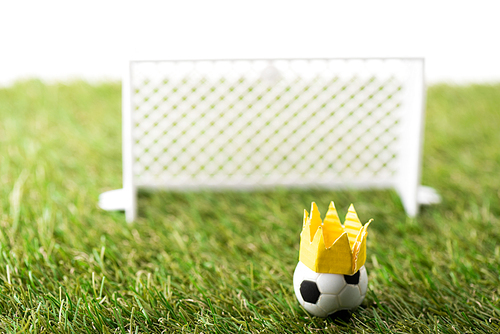 selective focus of toy football gates and ball with paper crown on green grass isolated on white, sports betting concept