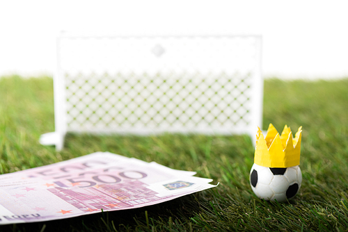selective focus of toy soccer ball with paper crown near euro banknotes and miniature gates isolated on white, sports betting concept