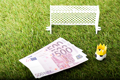 toy soccer ball with paper crown near euro banknotes and miniature gates, sports betting concept