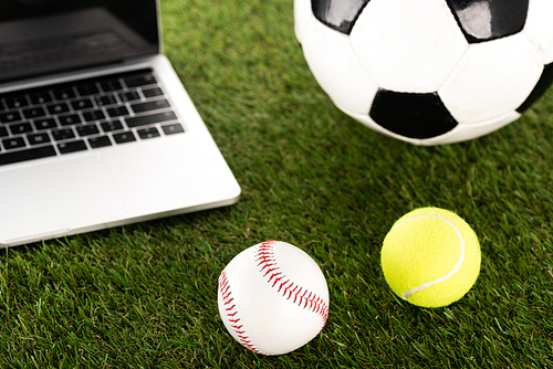 soccer, baseball and tennis balls near laptop on green grass, sports betting concept