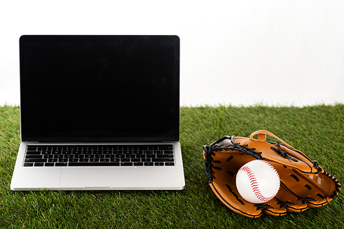 baseball glove and ball near laptop with blank screen on green grass isolated on white, sports betting concept