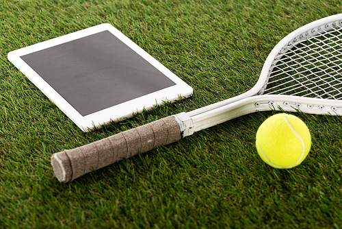 tennis racket and ball near digital tablet with blank screen on green grass, sports betting concept