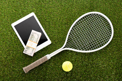 top view of tennis racket and ball near digital tablet and euro banknotes on green grass, sports betting concept
