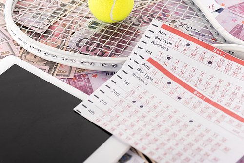digital tablet, betting lists, tennis racket and ball on euro and dollar banknotes, sports betting concept
