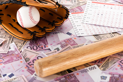 betting lists near baseball bat, glove and ball on euro and dollar banknotes, sports betting concept