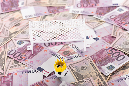 toy soccer ball with paper crown near miniature football gates on euro and dollar banknotes, sports betting concept
