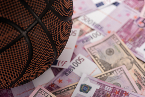 close up view of basketball ball on euro and dollar banknotes, sports betting concept
