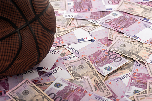 close up view of basketball ball on euro and dollar banknotes, sports betting concept