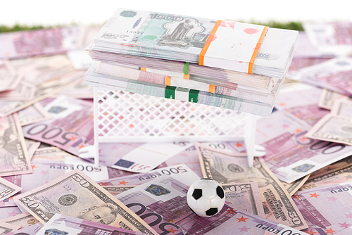 miniature soccer ball and gates near packs of money on euro and dollar banknotes isolated on white, sports betting concept