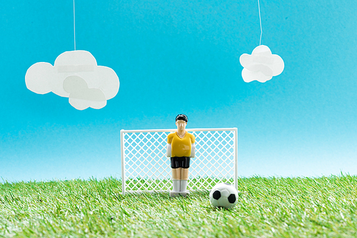 football field with toy goalkeeper near miniature football on blue background with clouds, sports betting concept