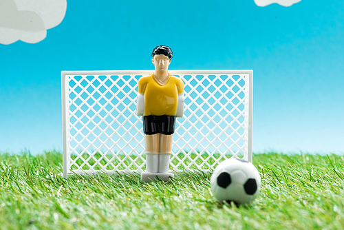 toy goalkeeper near miniature football gates and ball on blue background with clouds, sports betting concept
