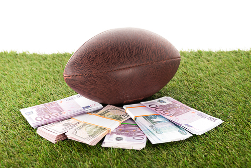 rugby ball near packs of euro and dollar banknotes on green grass isolated on white, sports betting concept