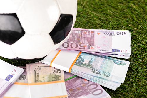 selective focus of packs of euro and dollar banknotes near soccer ball on green grass, sports betting concept