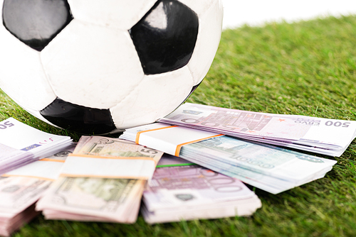 selective focus of euro and dollar banknotes near soccer ball on green grass, isolated on white, sports betting concept