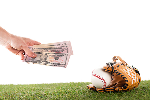 cropped view of female hand with dollar banknotes near baseball glove and ball on green grass isolated on white, sports betting concept