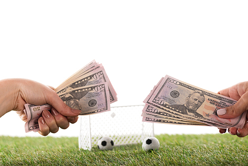 partial view of female hands with dollar banknotes near toy soccer balls and gates on green grass isolated on white, sports betting concept