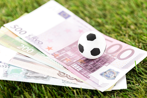 selective focus of toy soccer ball and euro banknotes on green grass, sports betting concept