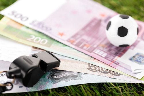selective focus of whistle, toy soccer ball and euro banknotes on green grass, sports betting concept