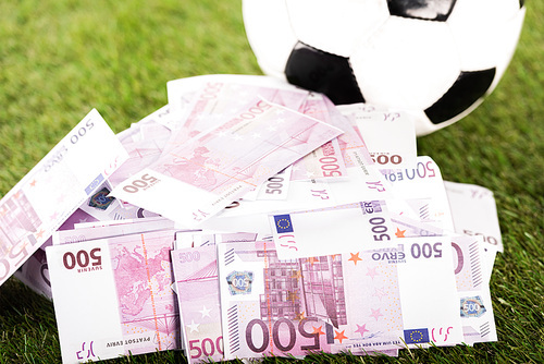 euro banknotes near soccer ball on green grass, sports betting concept