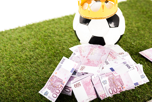 euro banknotes near soccer ball with paper crown on green grass isolated on white, sports betting concept