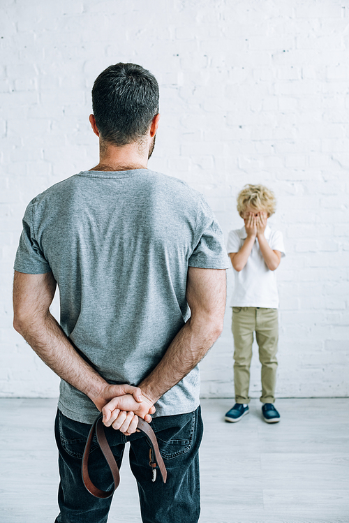 back view of father with belt and scared son at home