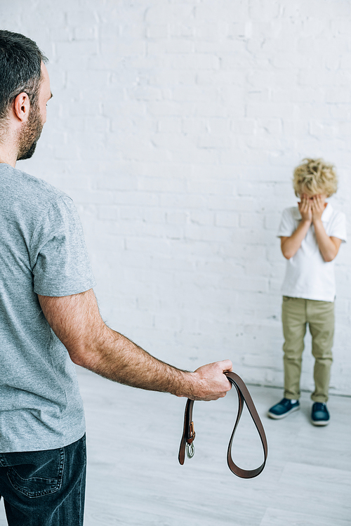 cropped view of father with belt and crying son at home