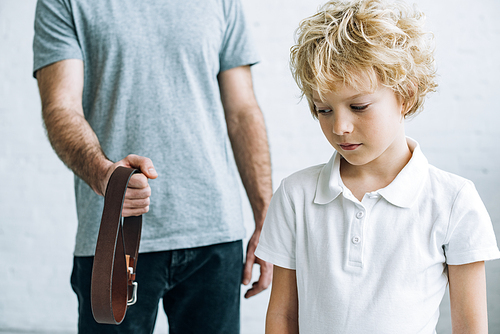 cropped view of father with belt and upset son at home