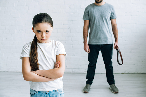 cropped view of father holding belt and upset daughter at home