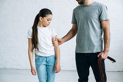 partial view of father with belt in hand grabbing daughter at home