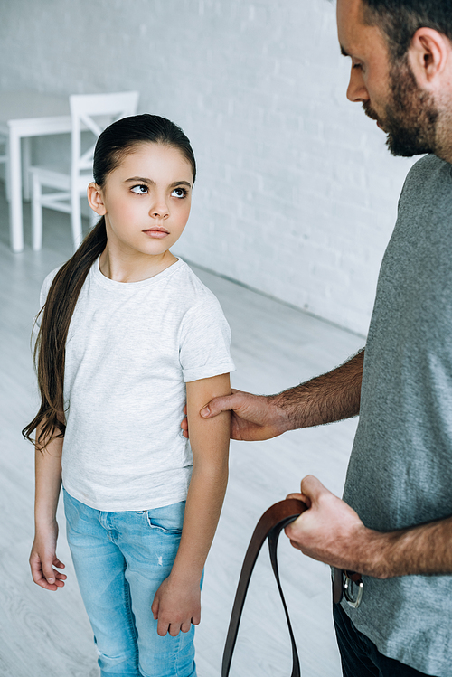 partial view of father with belt in hand grabbing daughter at home